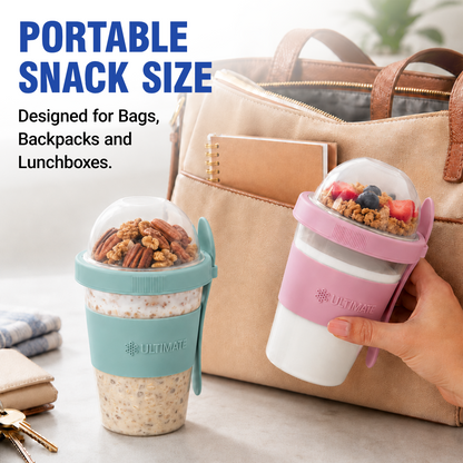 Two portable snack-size Yogurt Parfait Cups from Ultimate are shown on a tabletop beside a beige tote bag. One container has a teal sleeve and lid, filled with granola and pecans, and the other has a pink sleeve and lid, filled with yogurt and fruit.